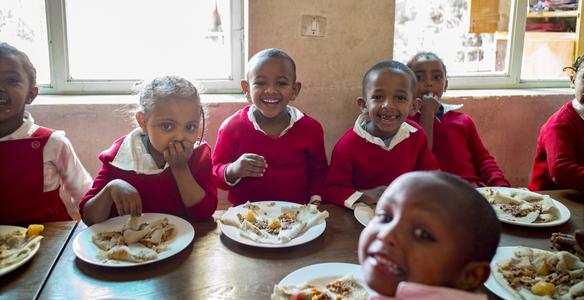 Äthiopische Kinder in Schuluniform lachen und sitzen beim Mittagessen.