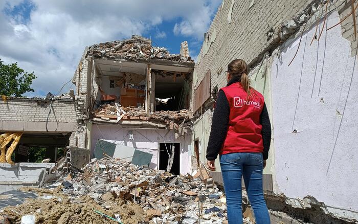 humedica-Mitarbeiterin vor zerstörten Gebäuden in der Ukraine