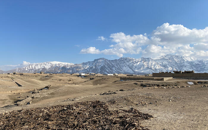 Schneebedeckte Berge im Hintergrund, karge Landschaft mit entfernt sichtbaren Mauern im Vordergrund
