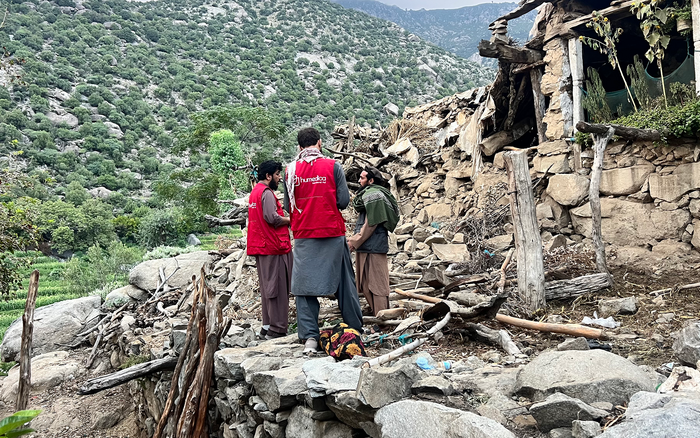 Zwei Männer mit humedica-Westen sprechen mit einem Afghanen vor einem durch ein Erdbeben zerstörtes Haus