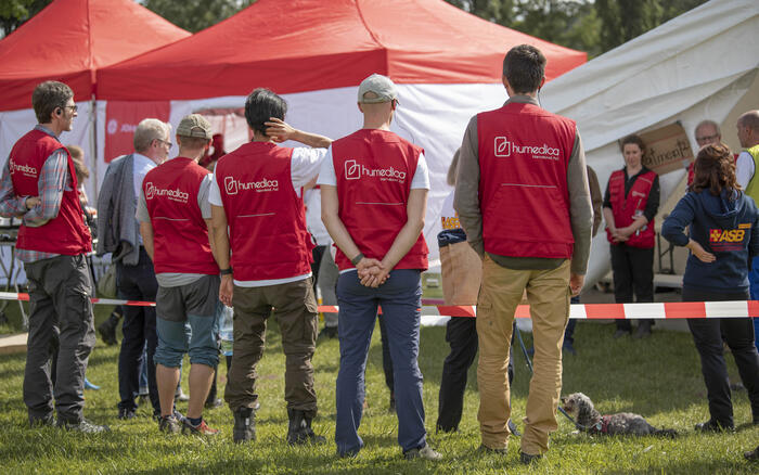 Vier Männer mit humedica-Westen stehen vor einem Absperrband und Zelten