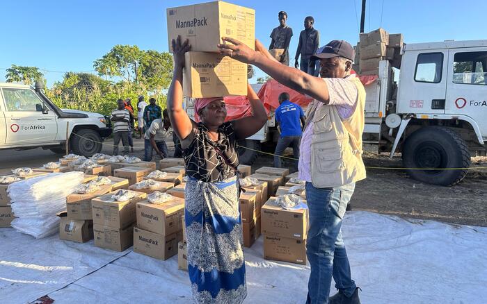 Eine Frau trägt zwei Kartons mit Lebensmitteln auf dem Kopf, ein Mann hilft beim Stabilisieren