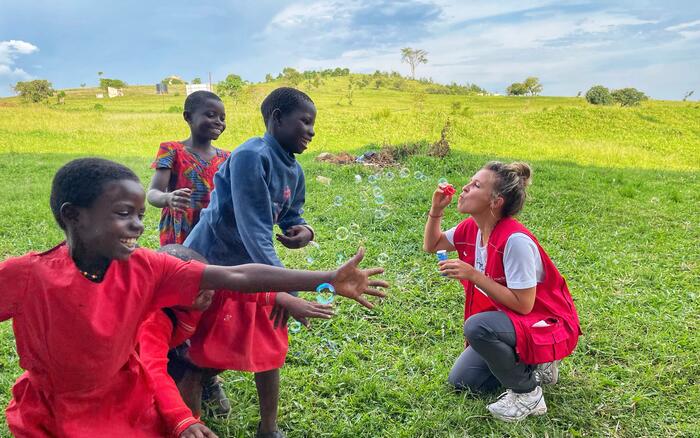 Drei Kinder freuen sich über Seifenblasen einer humedica-Einsatzkraft auf einer Wiese in Uganda