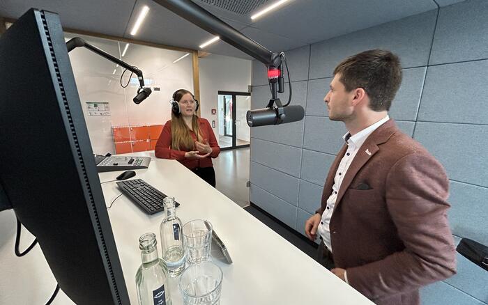 Ein Mann und eine Frau stehen in einem Studio vor Mikrifonen