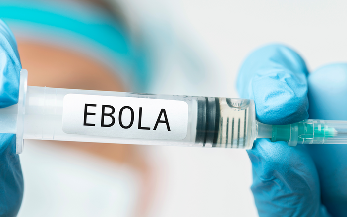 Hände mit blauen Handschuhen halten eine Spritze auf der EBOLA steht