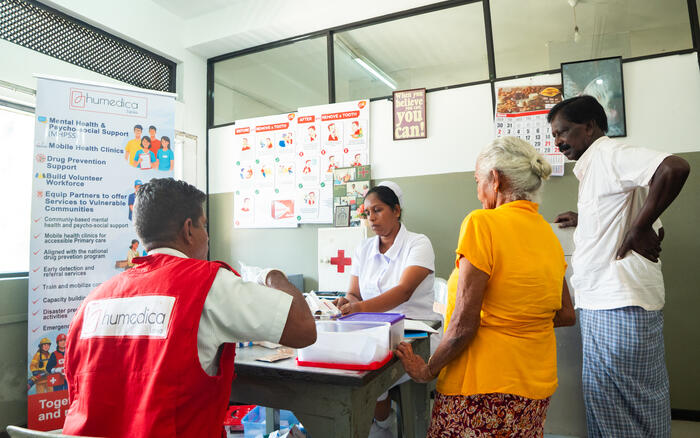 Eine Mitarbeiterin von humedica in roter Weste begleitet die medizinische Versorgung einer älteren Frau und eines Mannes in einer Gesundheitseinrichtung in Sri Lanka.