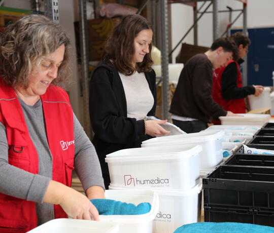 Menschen stehen in einer Reihe und packen Sachen in weiße Eimer mit der Aufschrift humedica