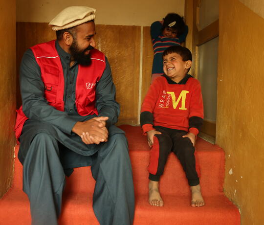 Ein Mann mit roter humedica-Weste und ein Junge sitzen auf einer Treppe und lachen