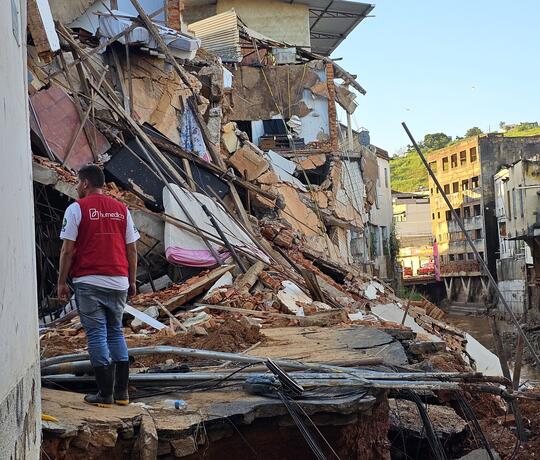 Ein Mann mit roter humedica-Weste steht nach einer Überschwemmung in Brasilien in einem zerstörtem Gebäudekomplex.