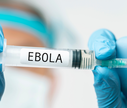 Hände mit blauen Handschuhen halten eine Spritze auf der EBOLA steht