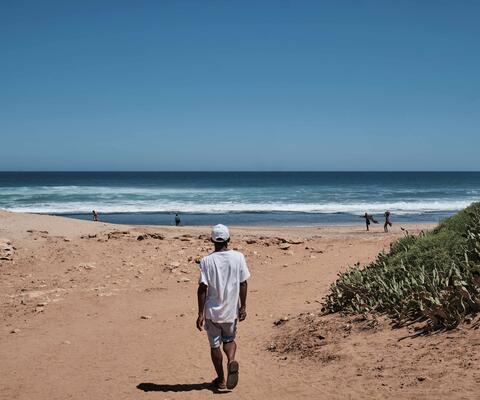 Ein Mann läuft am Strand auf das türkise Meer zu