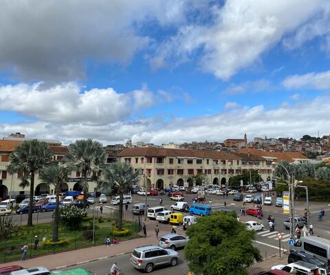 Das Stadtzentrum von Antananarivo mit einer großen Kreuzung, Autos, Häusern im Hintergrund und Palmen.