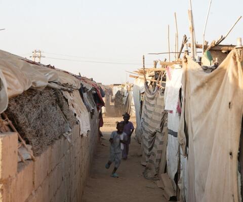 Zwei Kinder rennen durch einen schmalen Gang provisorischer Behausungen in einem Geflüchtetencamp