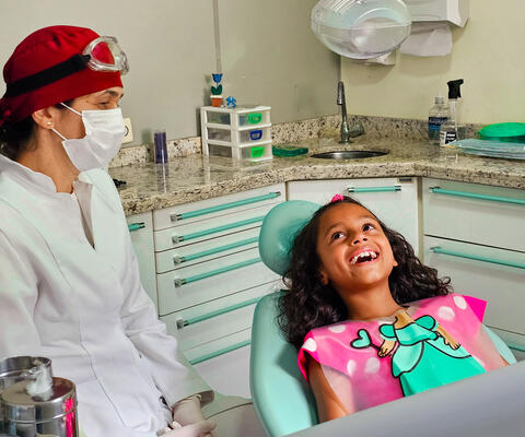 A Brazilian girl sits smiling in a dentist's chair next to a female dentist
