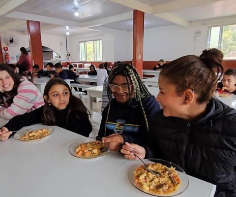 Four Brazilian girls sit in a canteen and talk during their meal