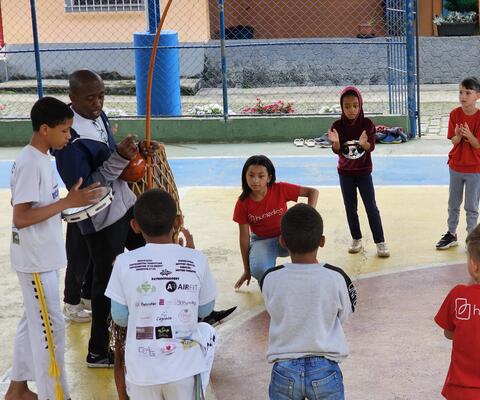 Children and trainers stand in a Capoeira circle in a gym