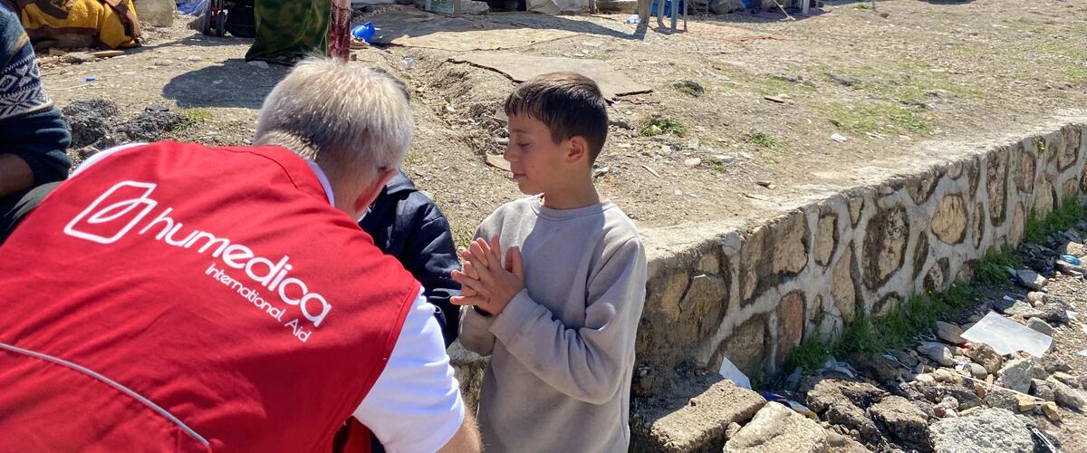 humedica Einsatzkraft unterhält sich mit zwei Jungen, im Hintergrund ist das Zeltlager zu sehen, das als Notunterkunft nach dem Erdbeben dient.