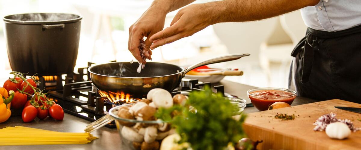 Ein Mann kocht und gibt etwas in die Pfanne