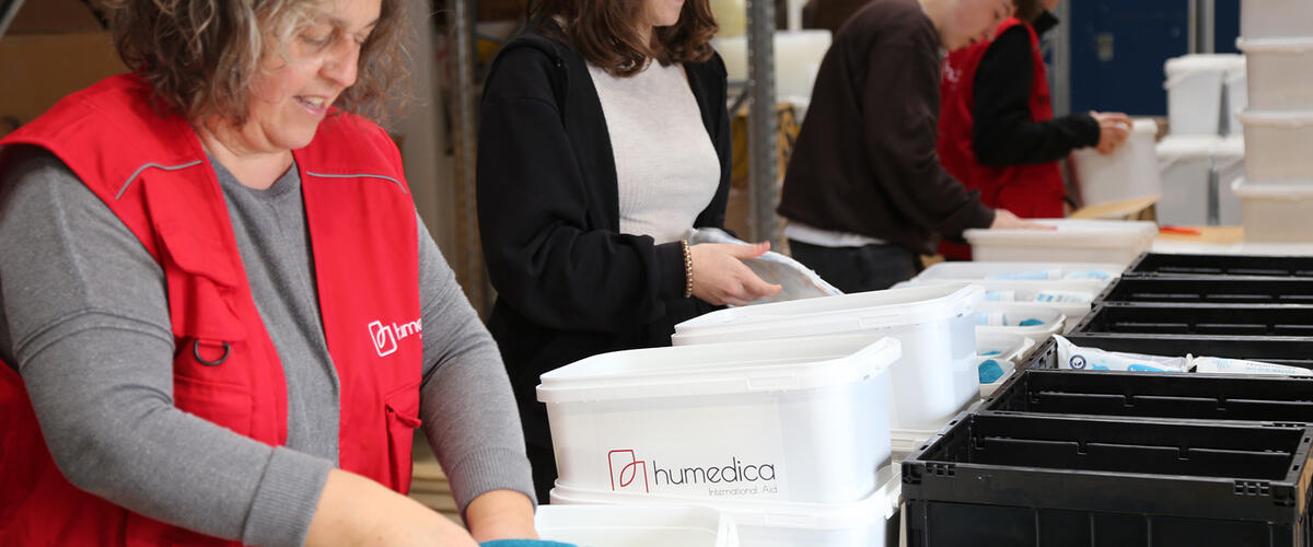 Vier Menschen stehen in einer Reihe und packen Materialien in weiße Boxen mit humedica-Logo