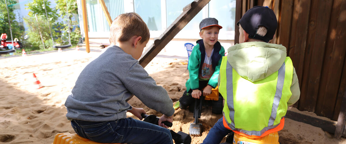 Drei Jungs spielen mit Baggerfahrzeugen im Sand