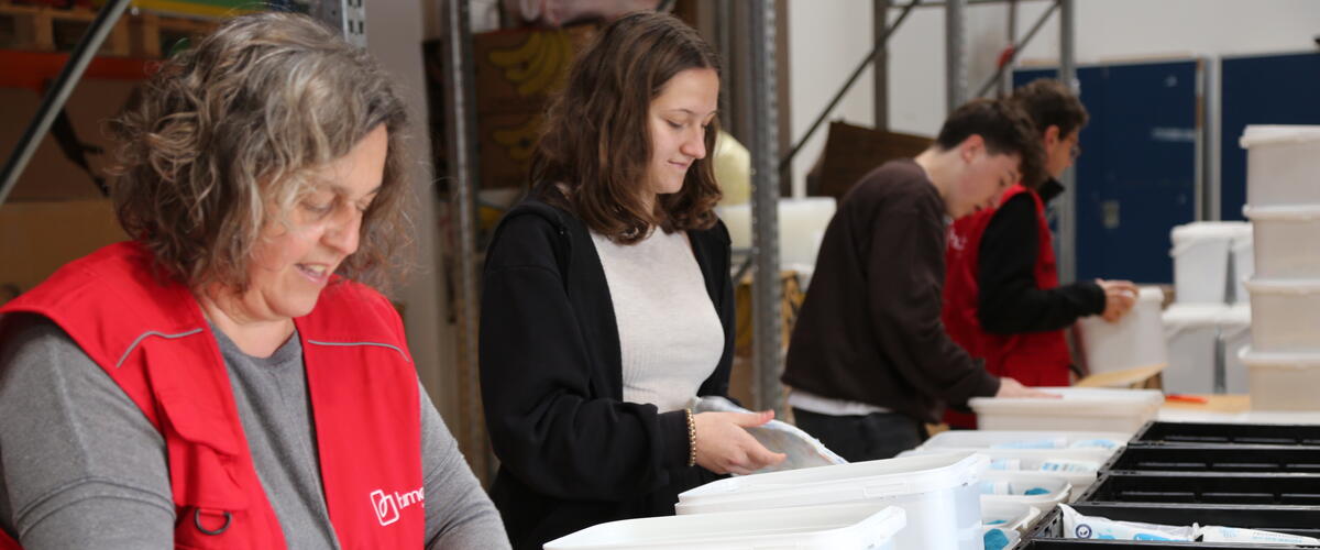 Menschen stehen in einer Reihe und packen Sachen in weiße Eimer mit der Aufschrift humedica