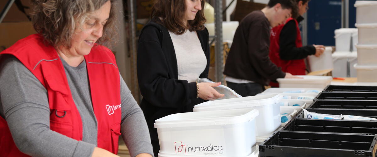 Menschen stehen in einer Reihe und packen Sachen in weiße Eimer mit der Aufschrift humedica