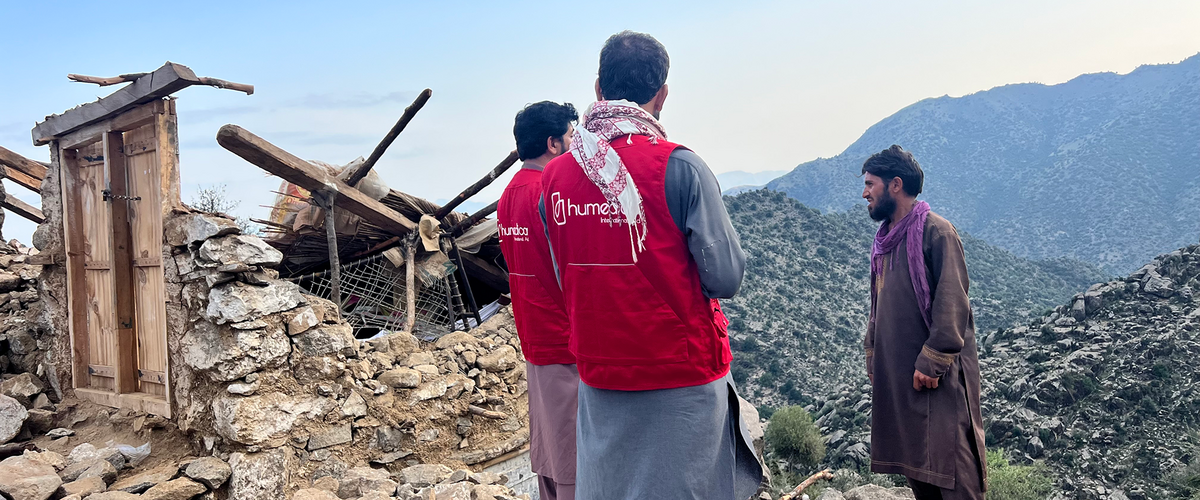 Zwei Männer mit humedica-Westen sprechen mit einem Afghanen vor einem durch ein Erdbeben zerstörtes Haus