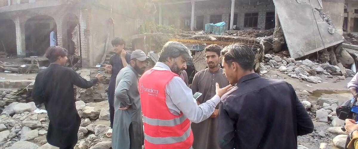 Ein Mann mit humedica-Weste spricht mit drei Männern inmitten von der Flut zerstörter Häuser in Pakistan