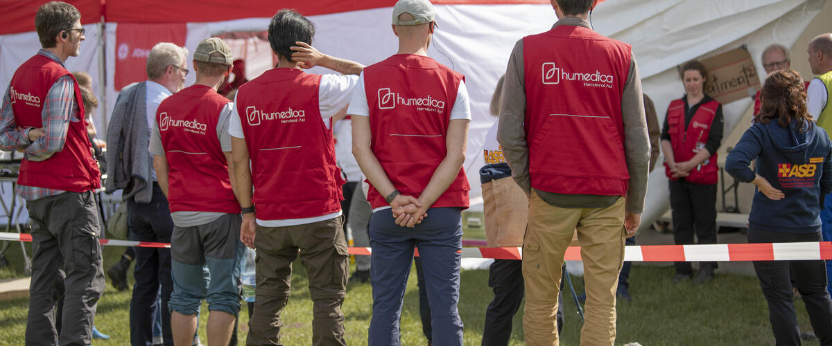 Vier Männer mit humedica-Westen stehen vor einem Absperrband und Zelten