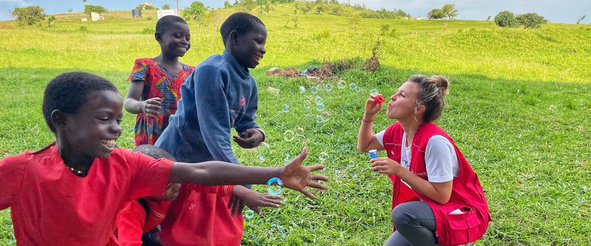 Drei Kinder freuen sich über Seifenblasen einer humedica-Einsatzkraft auf einer Wiese in Uganda