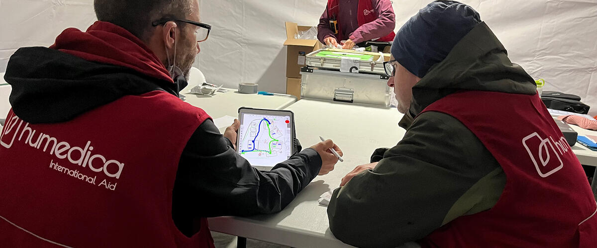 Drei humedica-Einsatzkräfte bereiten sich in einem Zelt vor, zwei davon sitzen vor einem Tablet mit einer Karte
