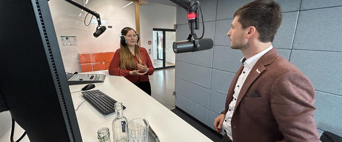 Ein Mann und eine Frau stehen in einem Studio vor Mikrifonen