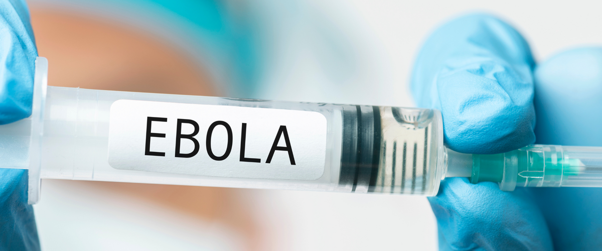 Hände mit blauen Handschuhen halten eine Spritze auf der EBOLA steht