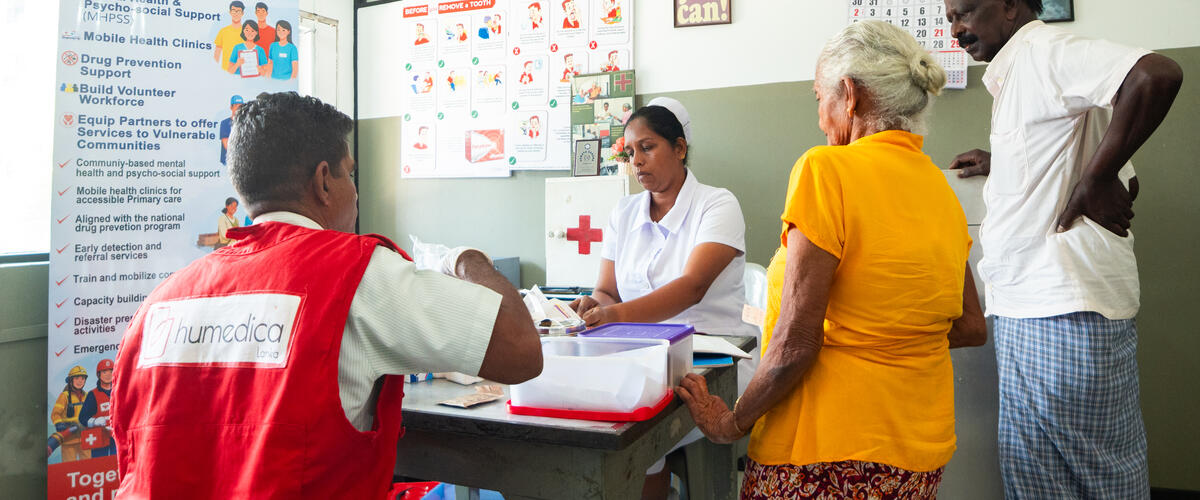 Eine Mitarbeiterin von humedica in roter Weste begleitet die medizinische Versorgung einer älteren Frau und eines Mannes in einer Gesundheitseinrichtung in Sri Lanka.