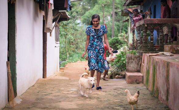 Mädchen läuft von Hund und Hühnern umgeben durch eine Gasse in Sri Lanka