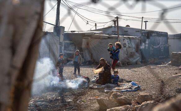 Frau und Kinder sitzen in einem Flüchtlingscamp im Libanon an Feuer