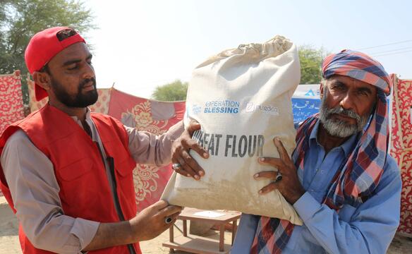 Ein Mann und ein Mitarbeiter halten Sack mit Nahrungsmitteln in Pakistan hoch