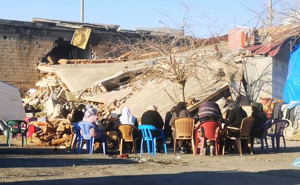 Menschen sitzen vor Häusertrümmern in der Türkei