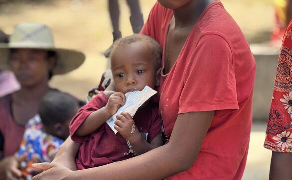 Ein Kind isst Aufbaunahrung auf dem Schoß der Mutter in Madagaskar