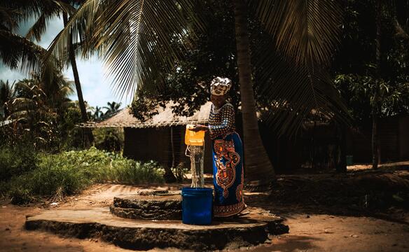 Eine Frau aus Mosambik leert sauberes Wasser in einen Behälter.