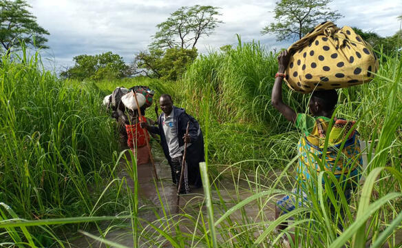 Menschen fliehen im Suedsudan durch Wasser umgeben von hohem Gras