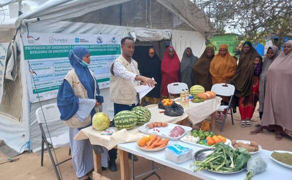 Verschleierte Frauen und ein Mann stehen um einen Tisch mit Lebensmitteln