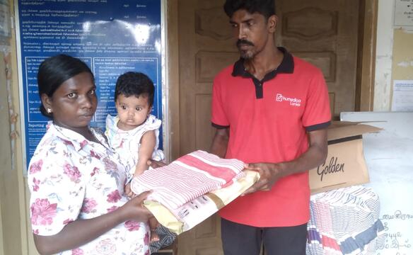 Ein Mann mit rotem humedica T-Shirt überreicht einer Frau mit Baby auf dem Arm eine Decke und ein Moskitonetz