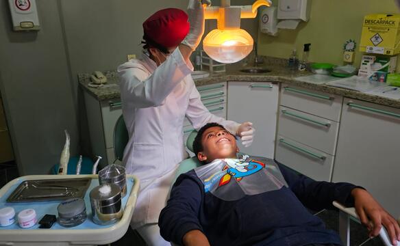 Ein Junge liegt in einem Zahnarztstuhl, die Zahnärztin stellt die Lampe über seinem Kopf ein