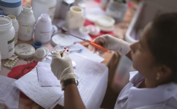 Ein Tisch mit Medikamenten über dem eine Frau mit der Schere einen Tablettenblister  auseinanderschneiden möchte