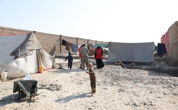 In einer Flüchtlingssiedlung sind Zelte zu sehen, dazwischen eine Gruppe Menschen und ein Kind, das in die Kamera schaut