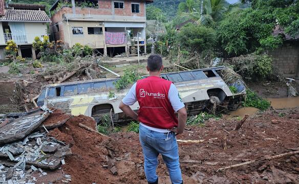 Nach einer Überschwemmung liegt ein umgekippter Bus neben einem Erdhaufen in einem Bach vor einem Haus