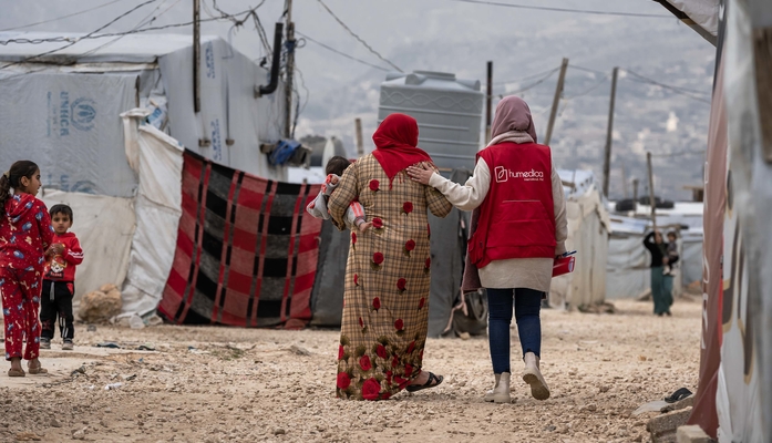 Frau läuft mit humedica-Mitarbeiterin durch das Flüchtlingscamp